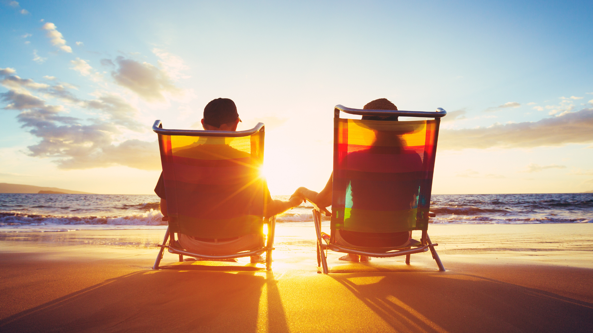 a man and a woman are sitting in beach chairs on the beach holding hands .