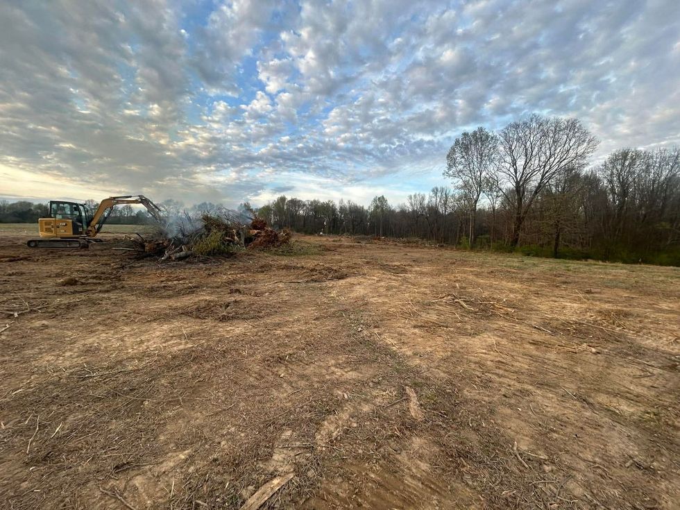 Bulldozer clearing brush on a dirt lot under a cloudy sky