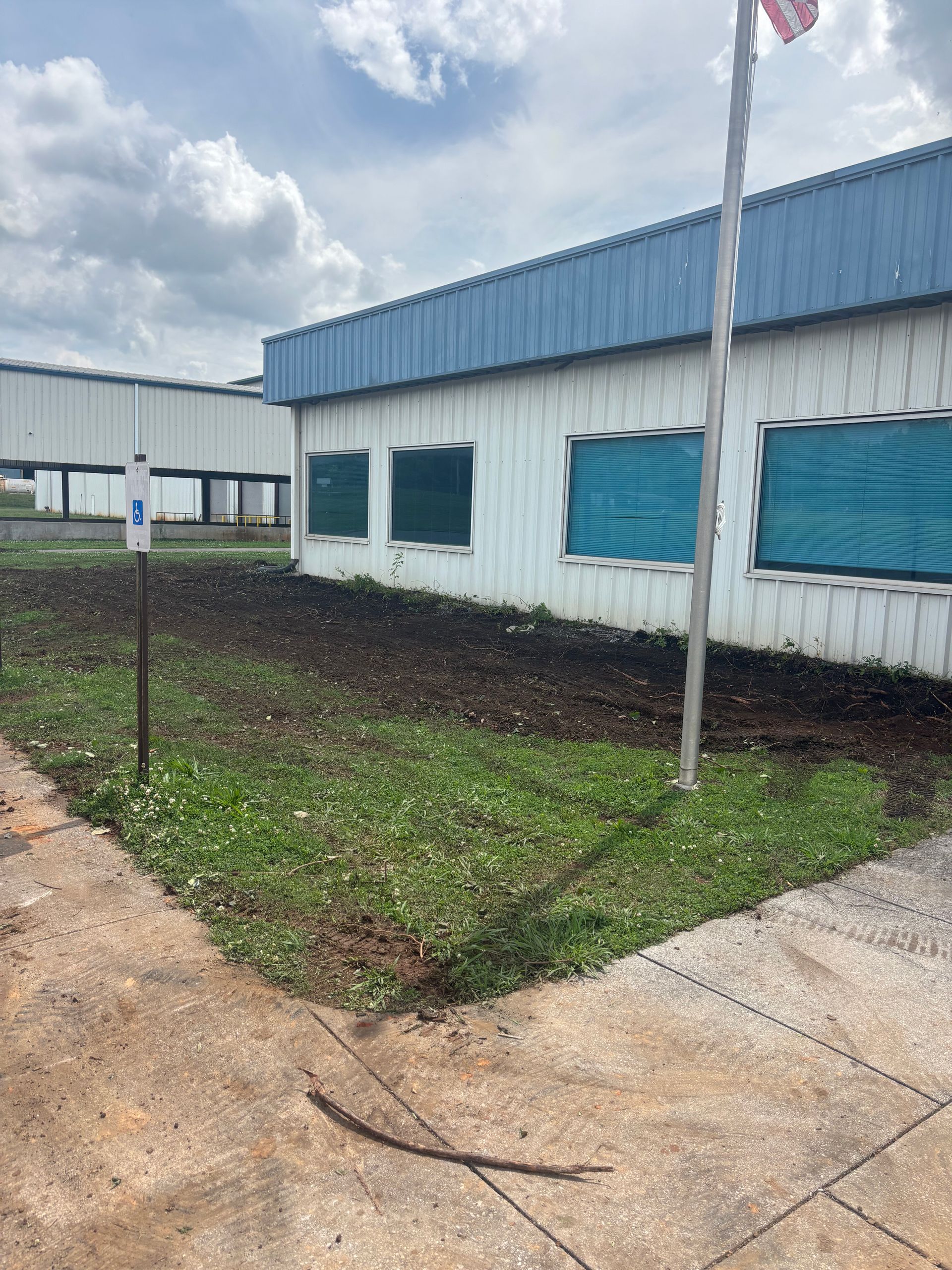 White industrial building with blue awnings, small grassy lot, and concrete walkway under cloudy sky