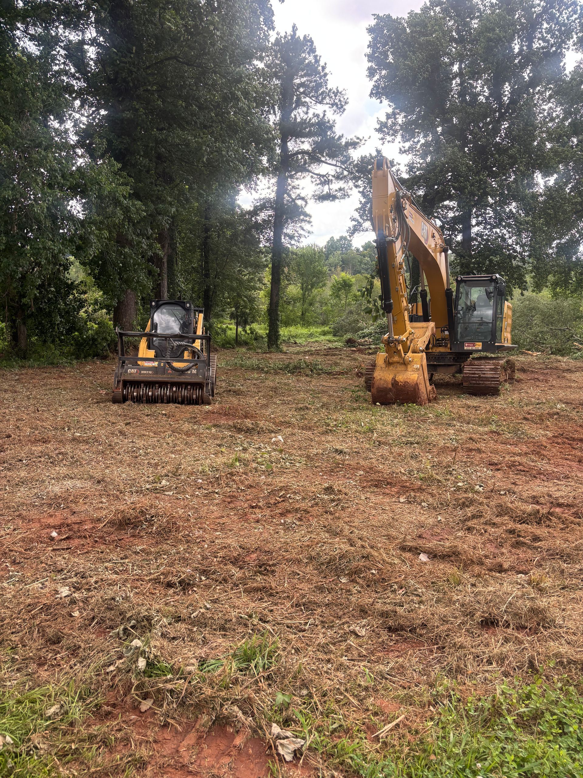 Two small excavators in a wooded clearing, one yellow machine with arm raised.