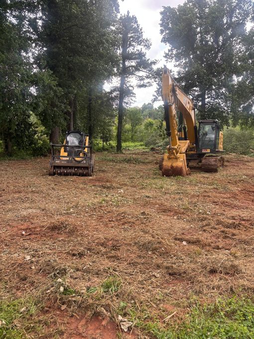 Two excavators working in a cleared wooded area with trees in the background