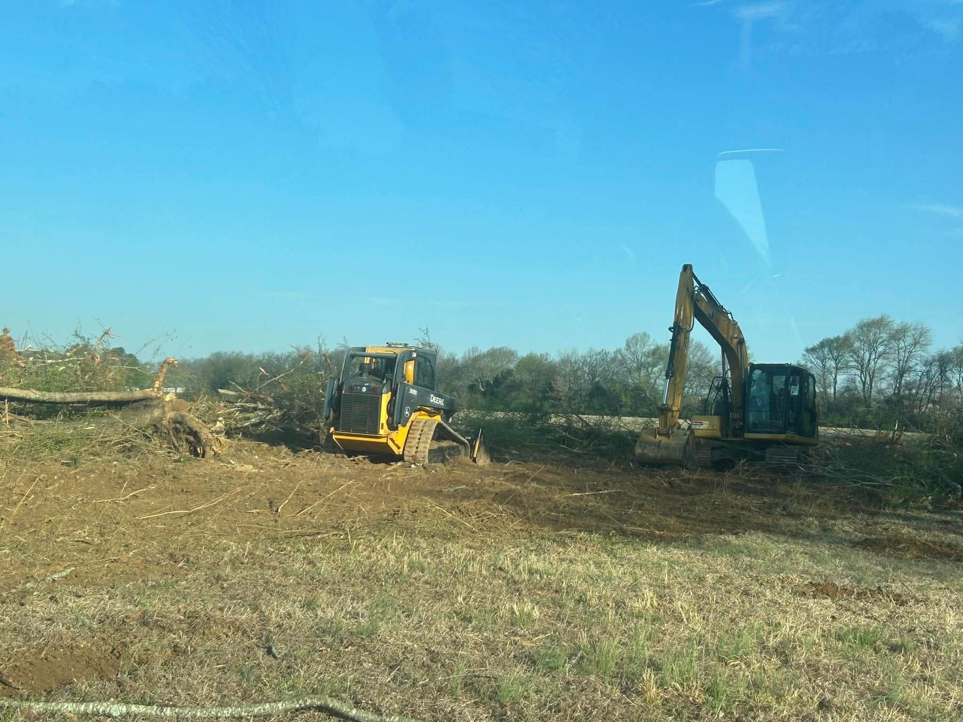 Excavator and yellow bulldozer working in a dry, open field under a clear blue sky