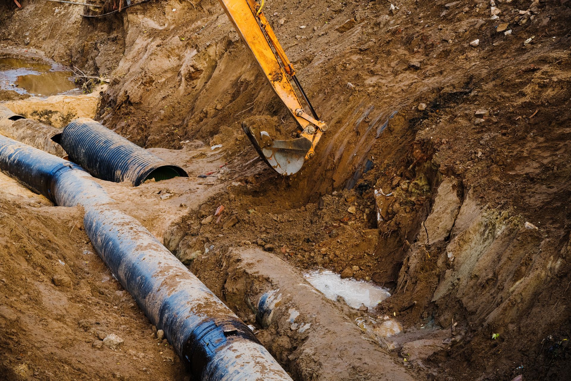 Excavator digging a trench beside large blue pipes at a construction site