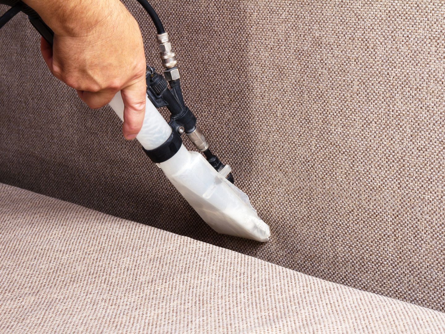 Hand using a vacuum cleaner nozzle to clean beige upholstery seam