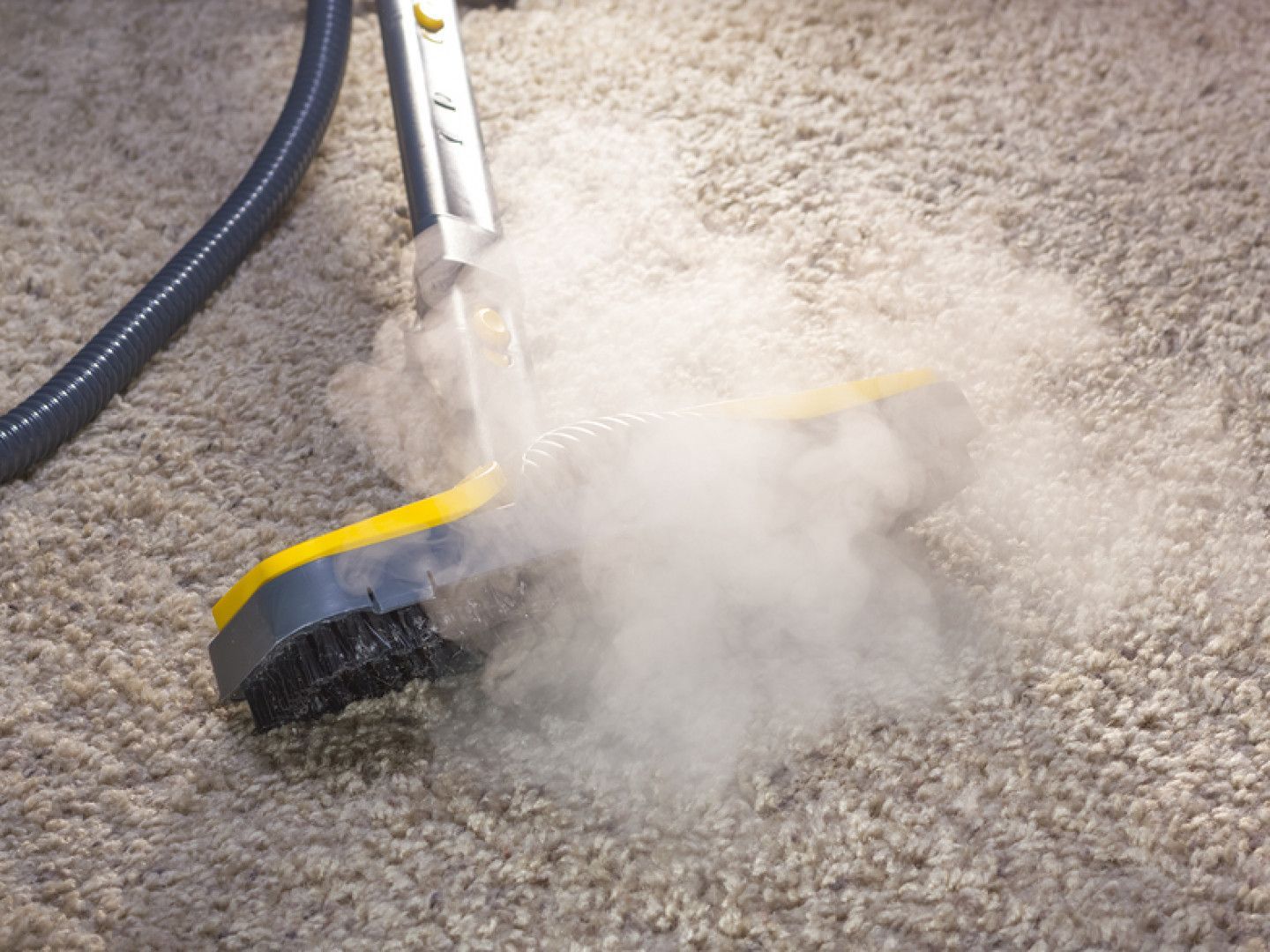 Yellow-and-black floor-cleaning tool spraying steam on a carpeted surface
