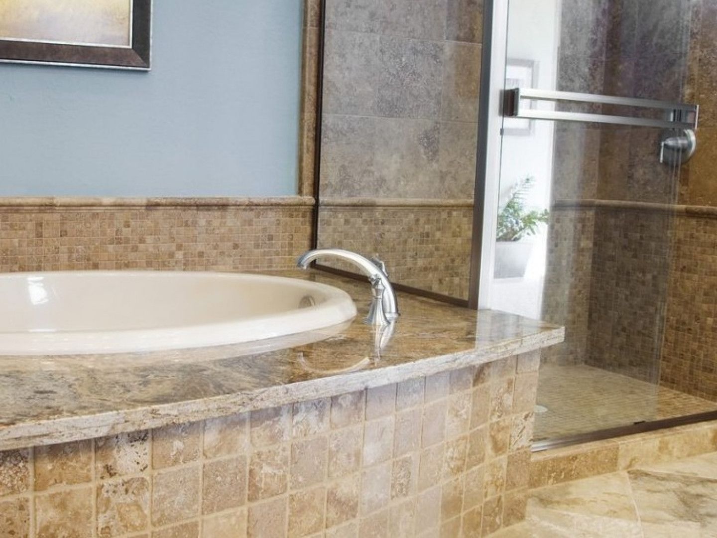 Bathroom vanity with a sink, tiled countertop, and partially visible bathtub beside a glass shower door.