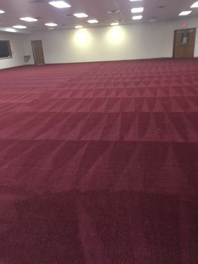 Empty room with maroon carpet, white walls, and a few doors and lights near the back wall