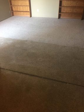 Empty carpeted room with beige walls and wooden shelves along the sides
