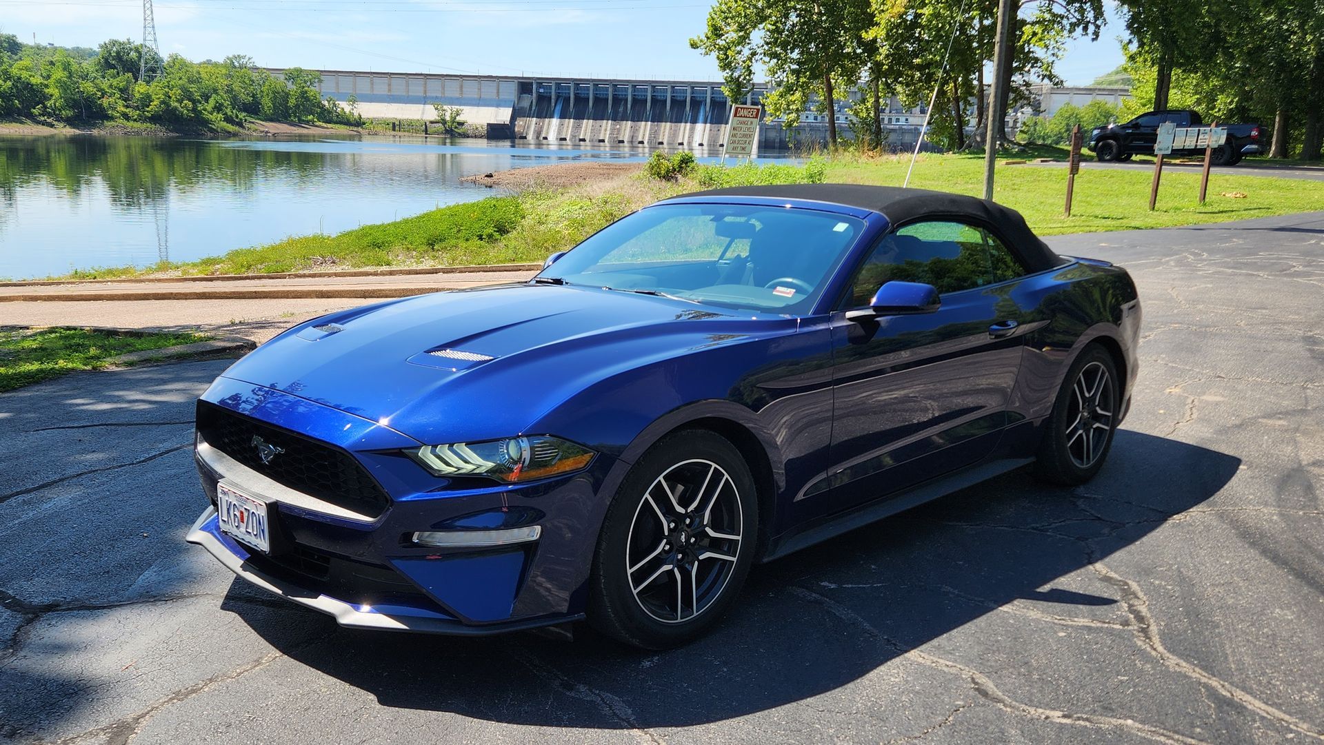 Blue convertible Mustang parked by a lakeside road on a sunny day.