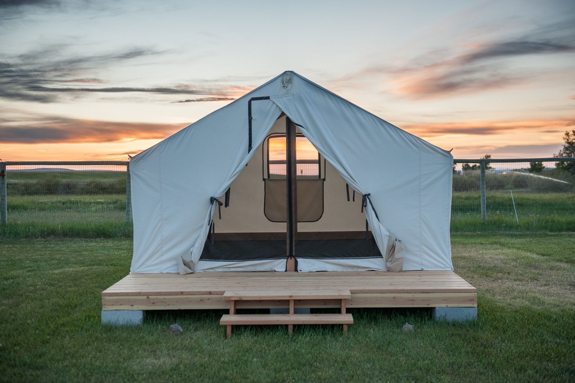 White canvas tent on a wooden platform with open entrance, set in grassy field at sunset.