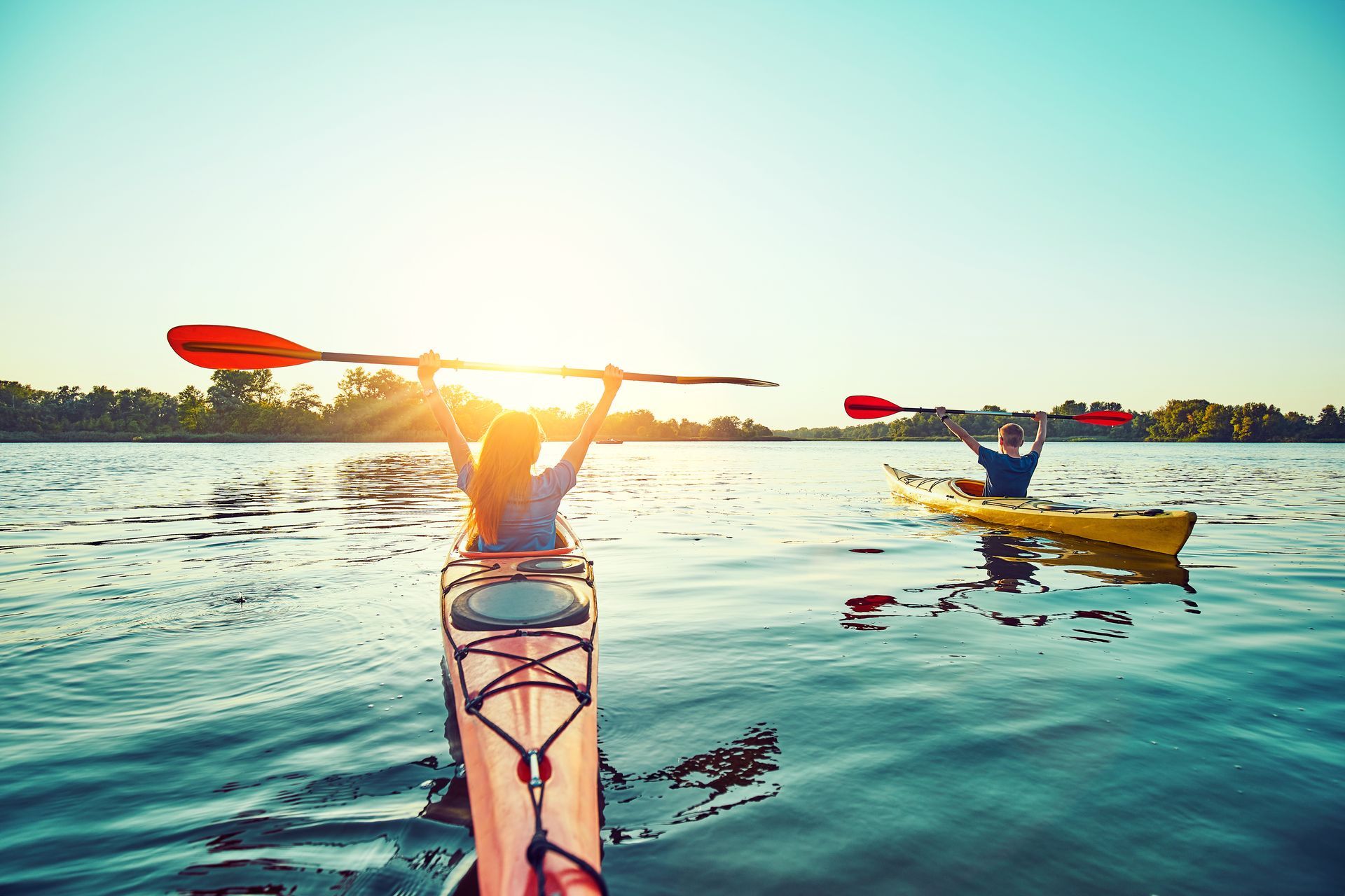 Two people kayaking on a sunny lake, one raising a paddle.