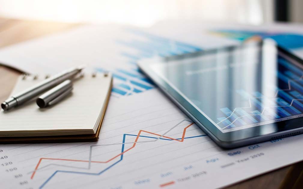 a tablet with a graph on it sits on a table next to a notebook and pens