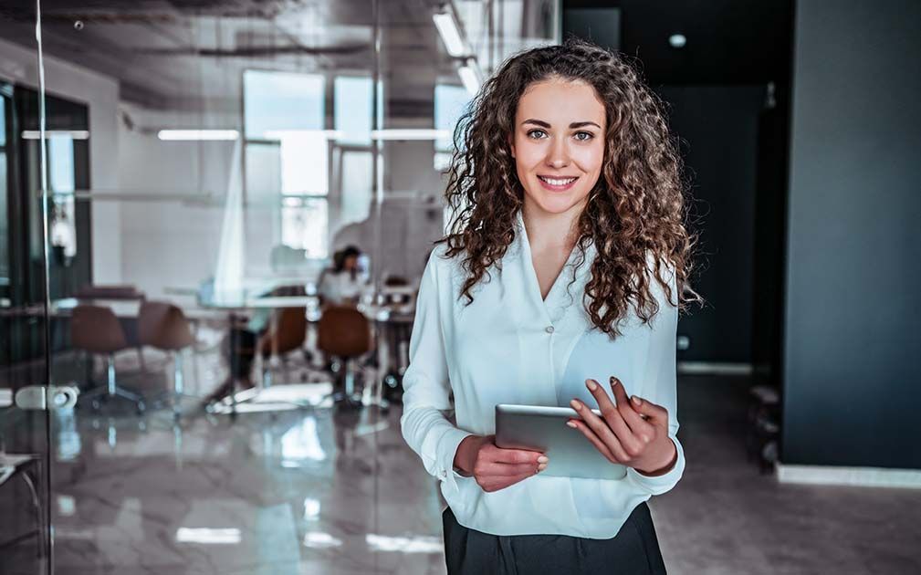 a woman with curly hair is holding a tablet and smiling