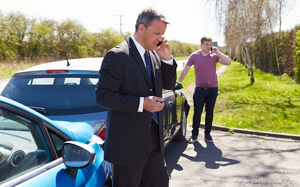 a man talking on a cell phone next to a blue car