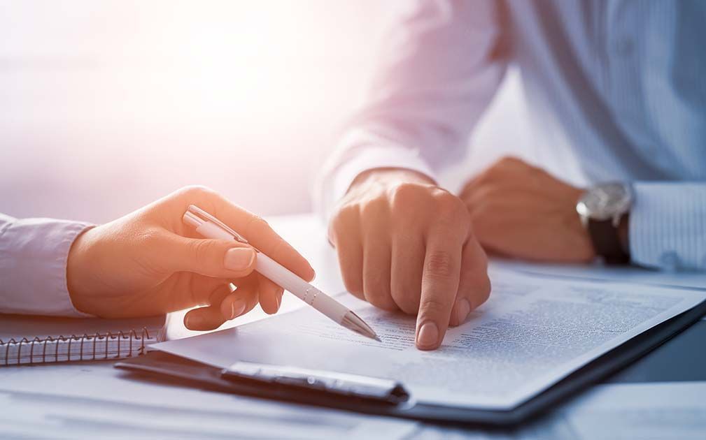 a person holding a pen pointing at a piece of paper