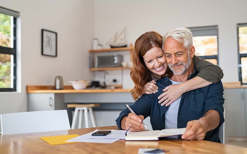 a woman is hugging a man while he writes in a notebook .