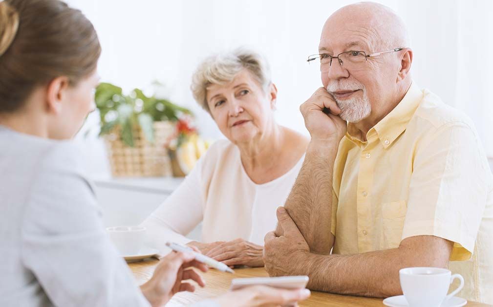 an elderly couple sit at a table with a woman holding a pen