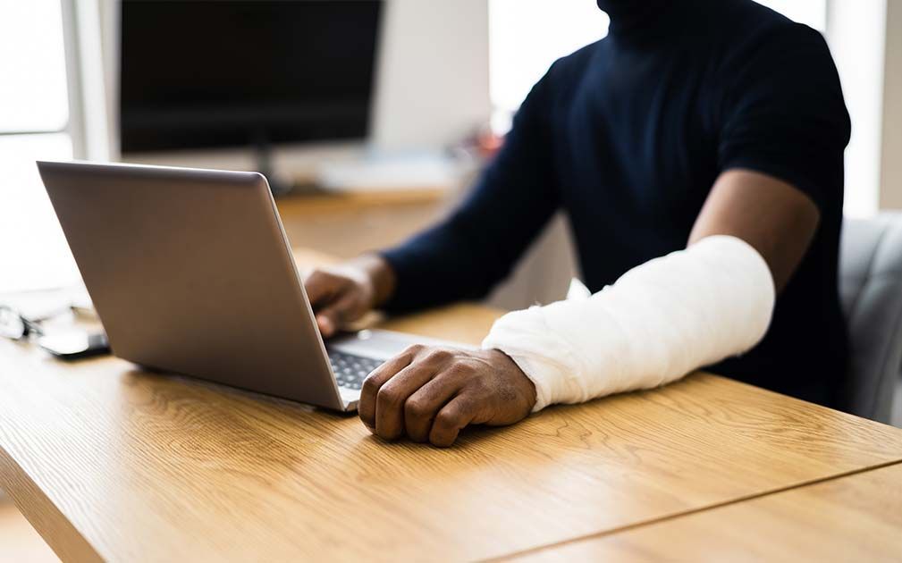 a man with a cast on his arm is typing on a laptop