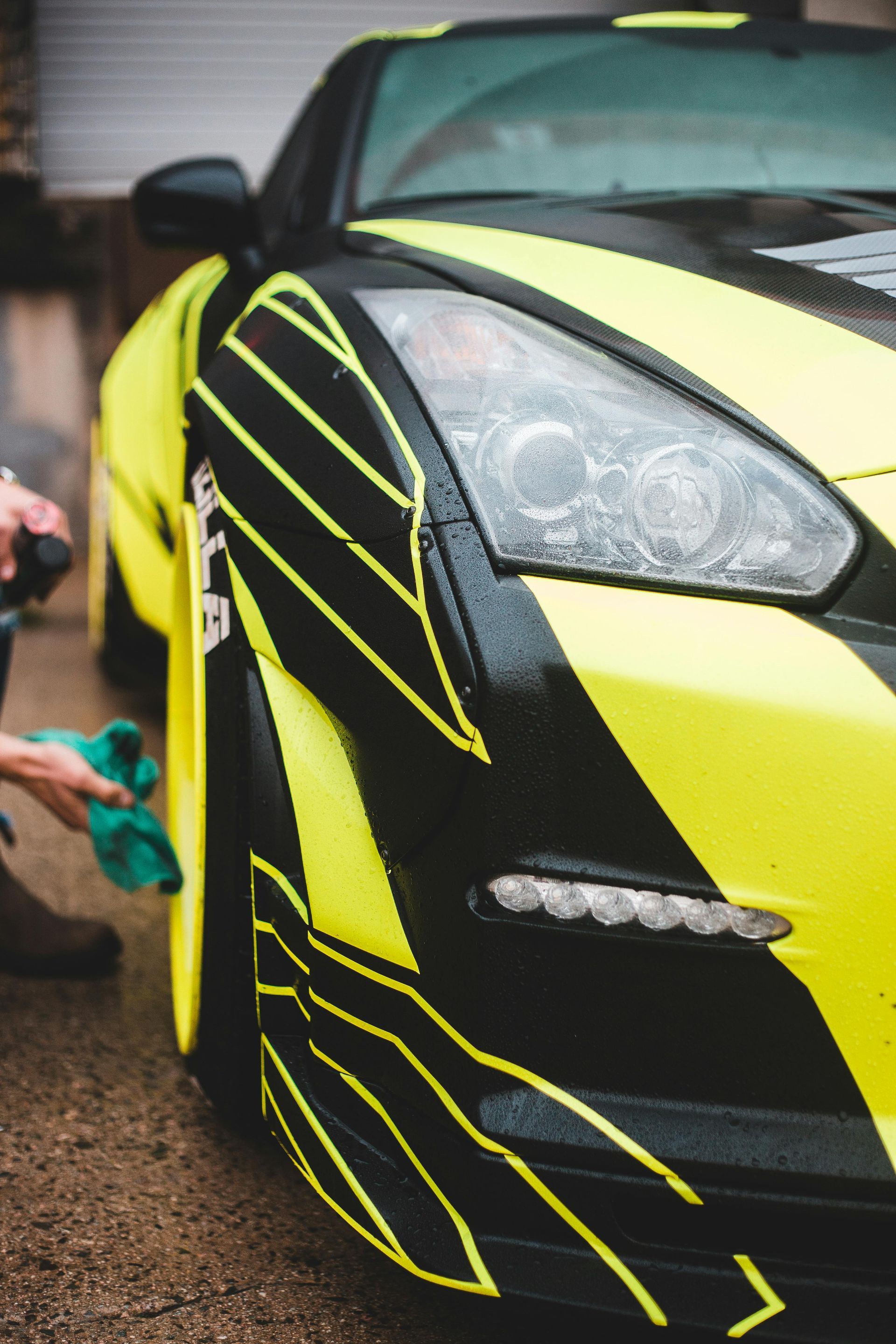 A person is cleaning a yellow and black sports car with a cloth.
