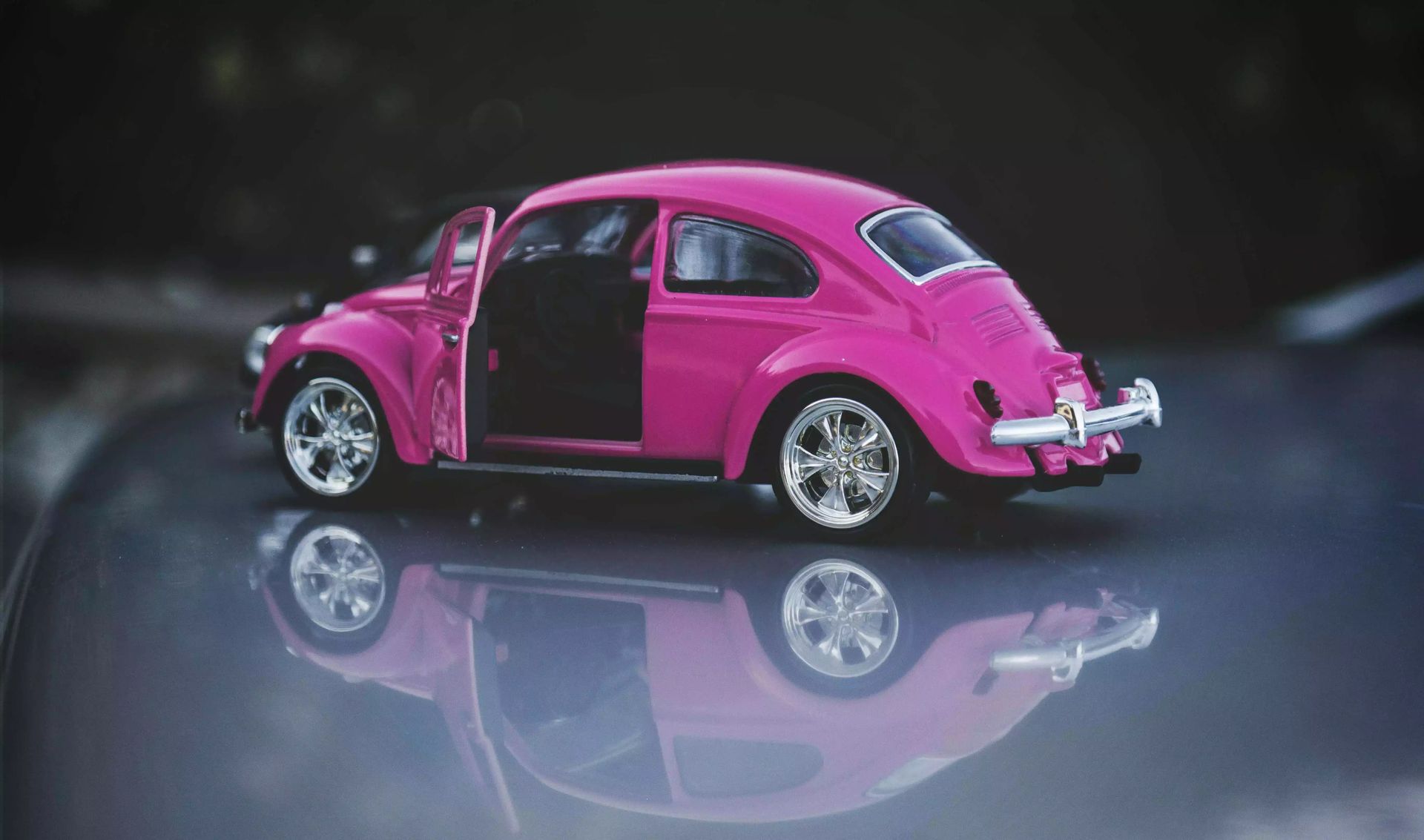 A pink toy car is sitting on top of a car with its doors open.