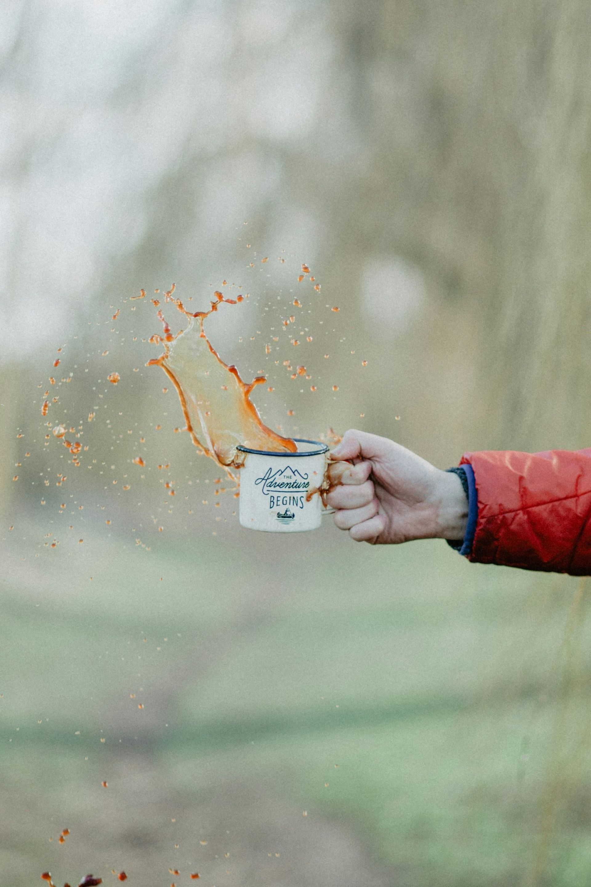 A person is holding a cup of coffee with coffee splashing out of it.