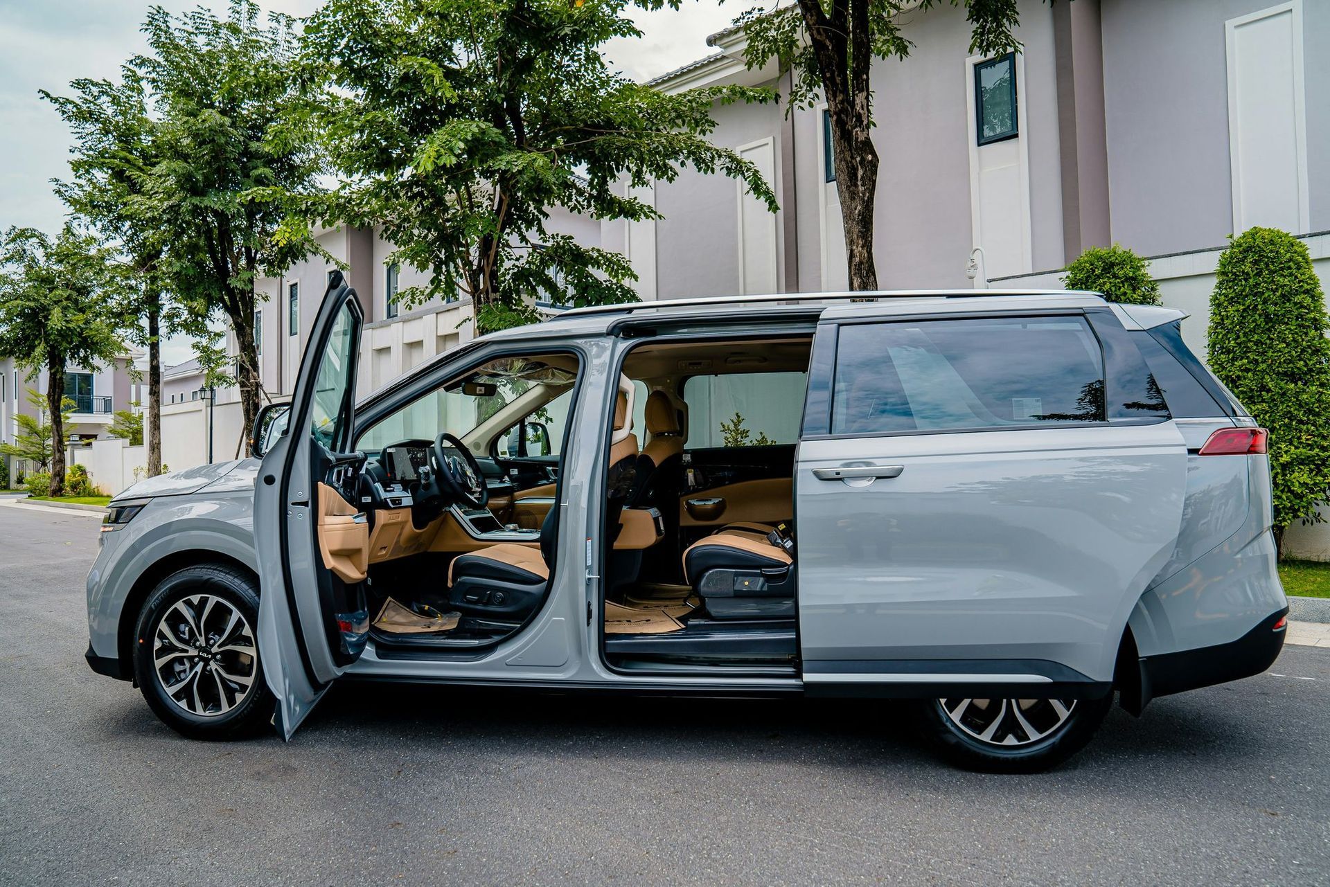 A silver minivan is parked on the side of the road with its doors open.