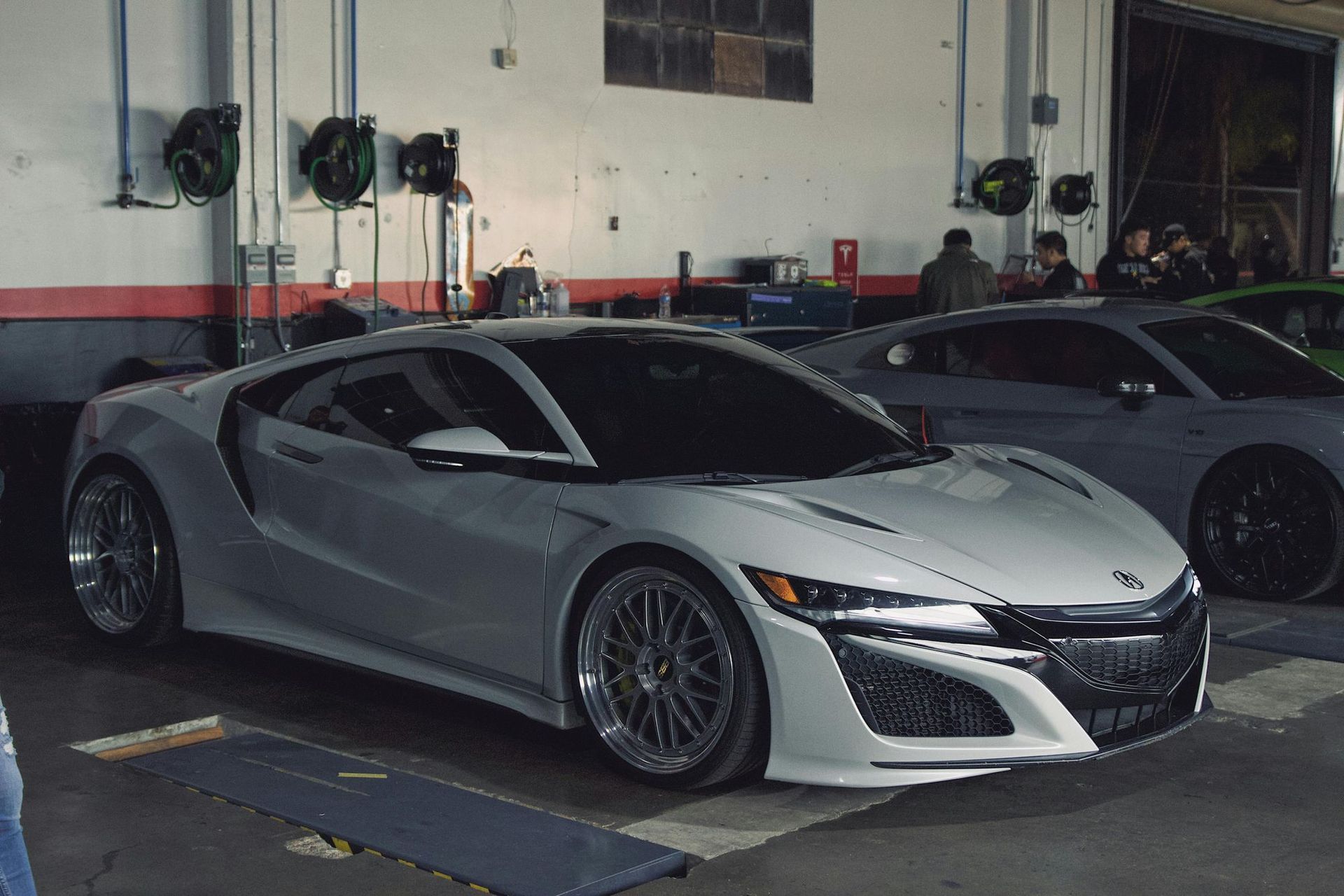 A silver sports car is parked in a garage next to a green sports car.