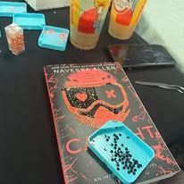 Book and craft supplies: book with bejeweled cover, plastic trays of rhinestones, beverages.
