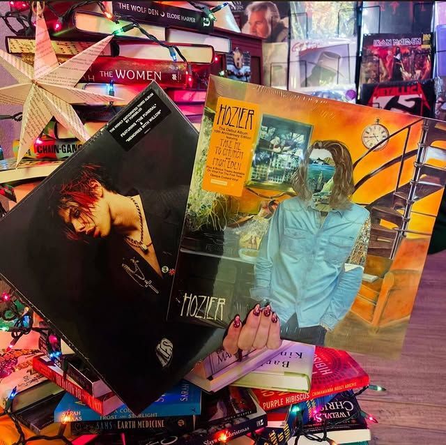 Assorted colorful vinyl album covers arranged on a pink surface with neon decor in the background