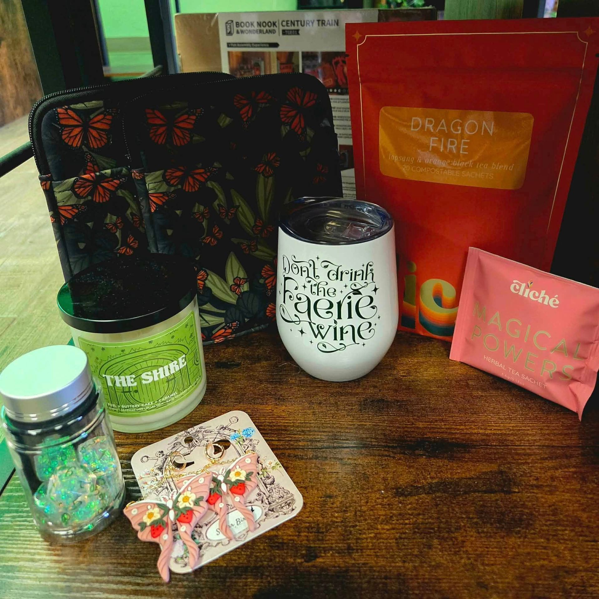 Assorted candle and bath gift items on a wooden table, including a red bag, jars, and a floral pouch