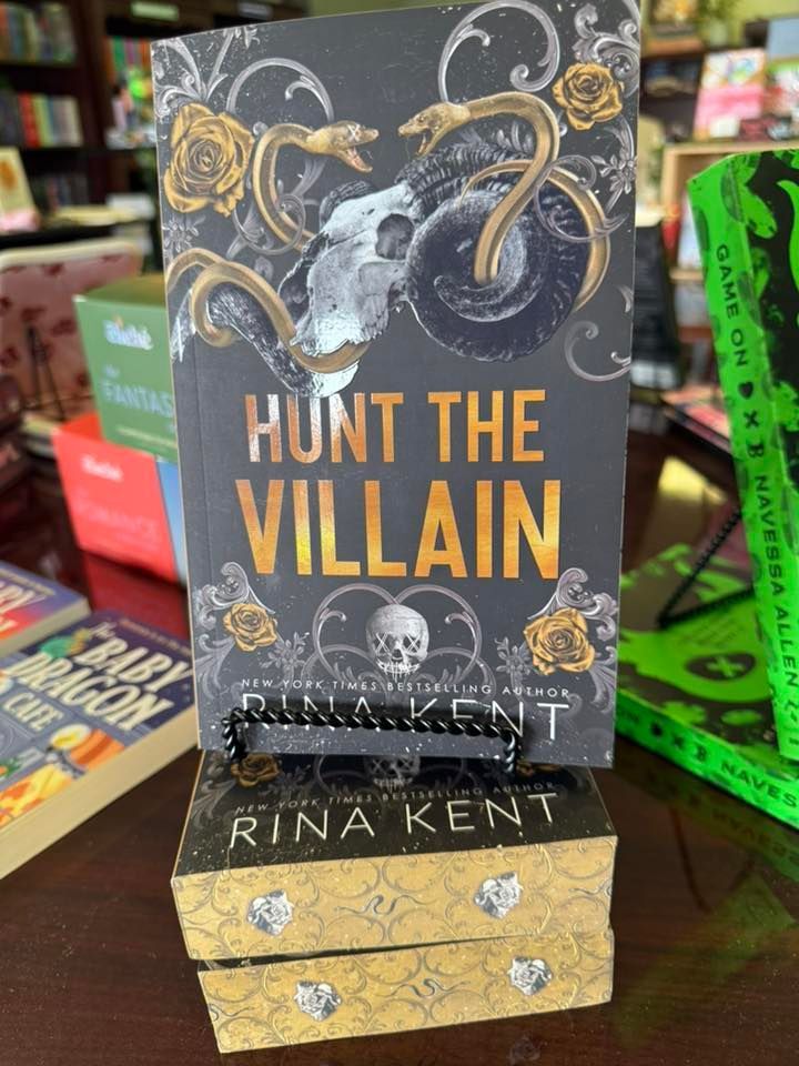 Tabletop display of the book “Hunt the Villain” by Rina Kent with dark cover art and gold accents