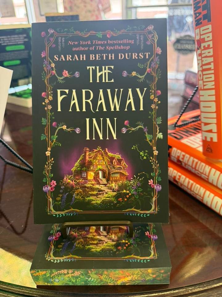 Book cover of “The Faraway Inn” by Sarah Beth Durst on a display stand, with a glowing cottage illustration.