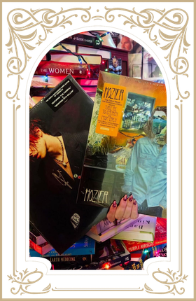 Decorative collage of magazines and books on a colorful surface, framed by an ornate gold border