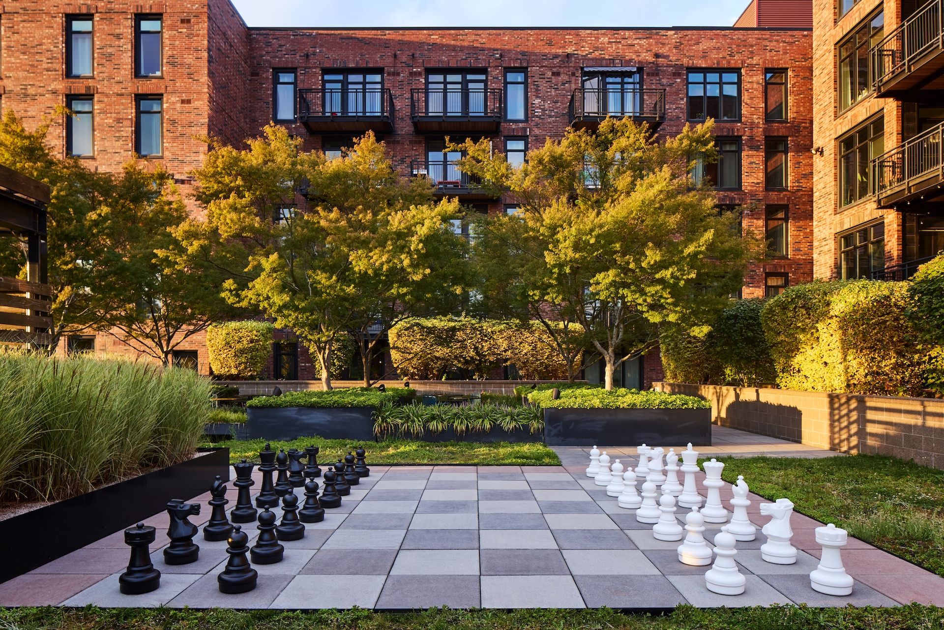 Outdoor chessboard in a courtyard between brick apartment buildings, with black and white pieces set up.