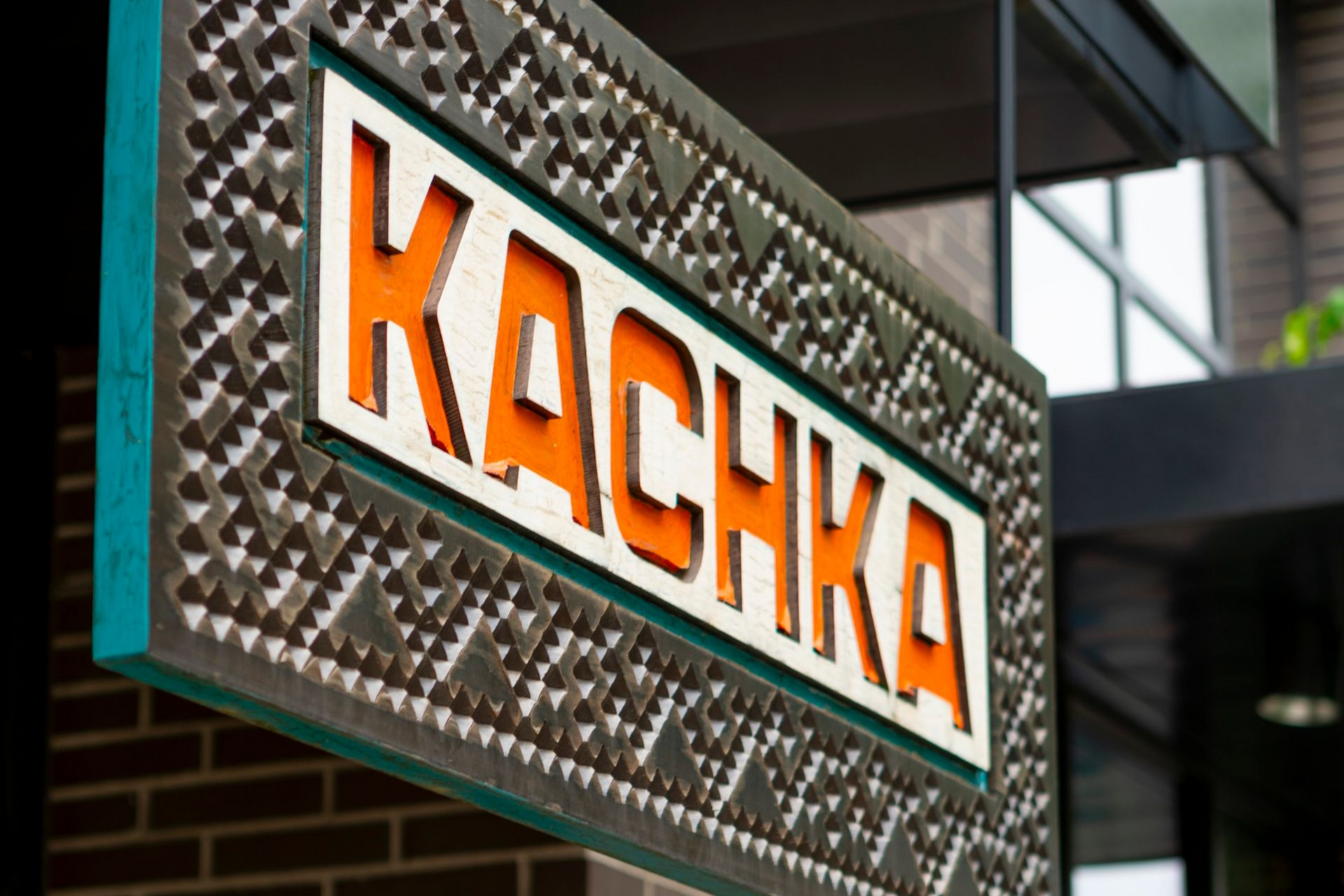 Orange “KACKA” sign on a brick building exterior with a decorative metal frame.