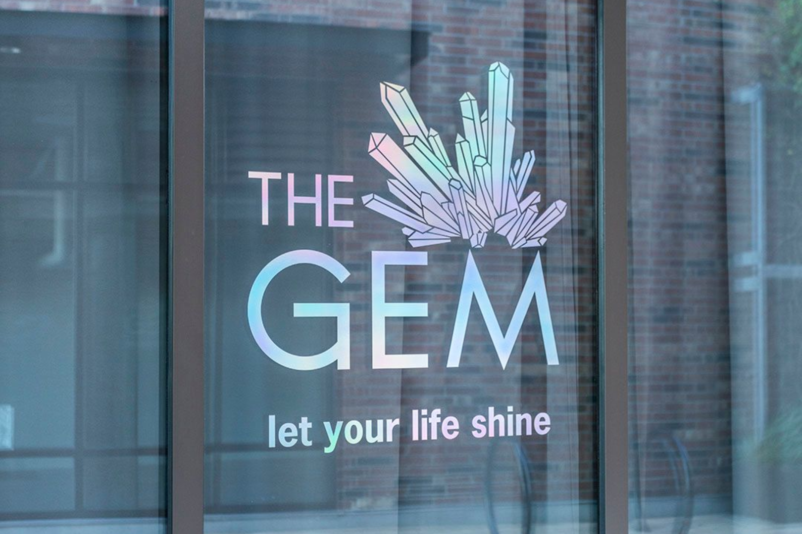 Storefront sign reading “THE GEM” with a crystal logo and the slogan “let your life shine”