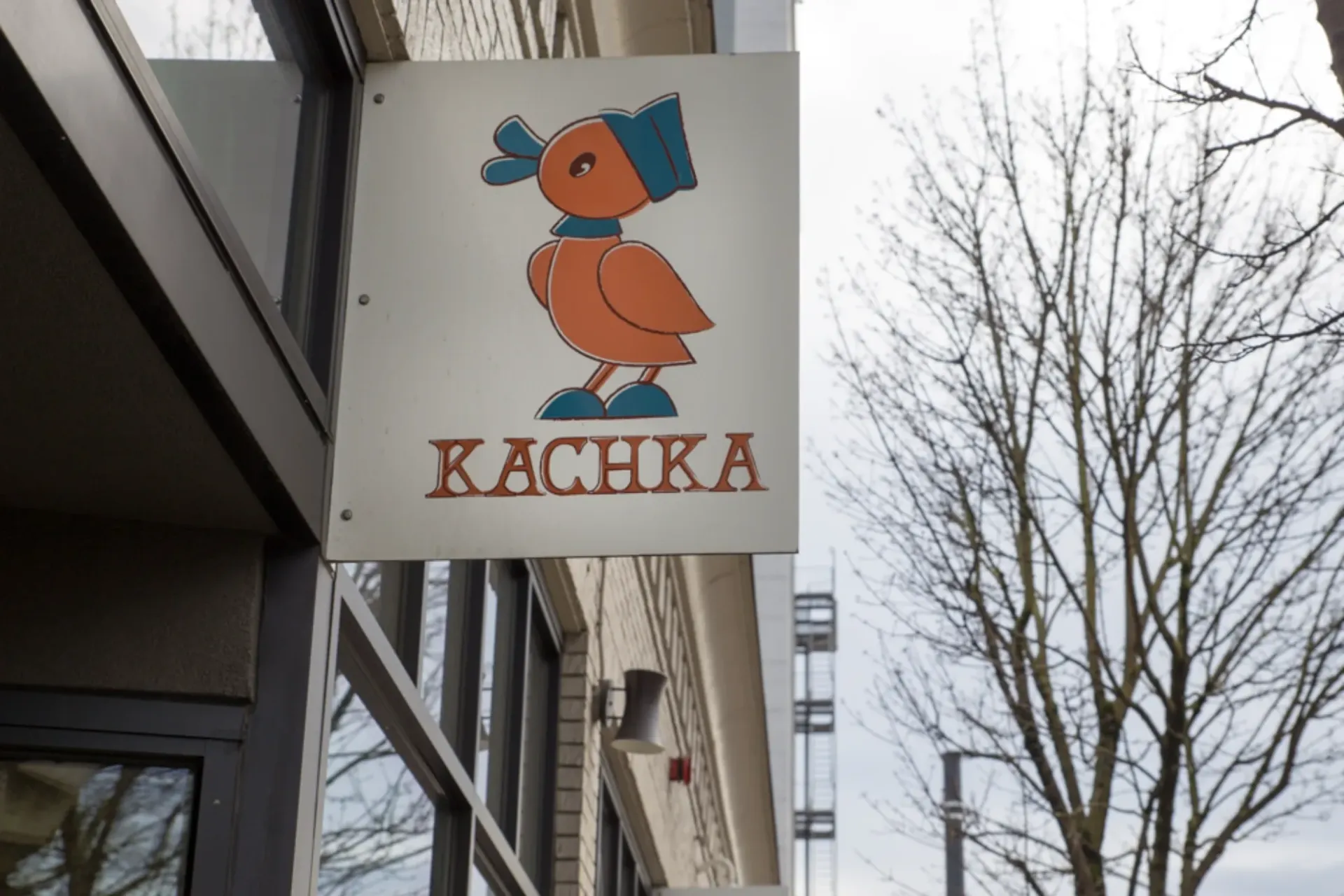 Sign for KACHKA restaurant with a cartoon orange duck on a city sidewalk