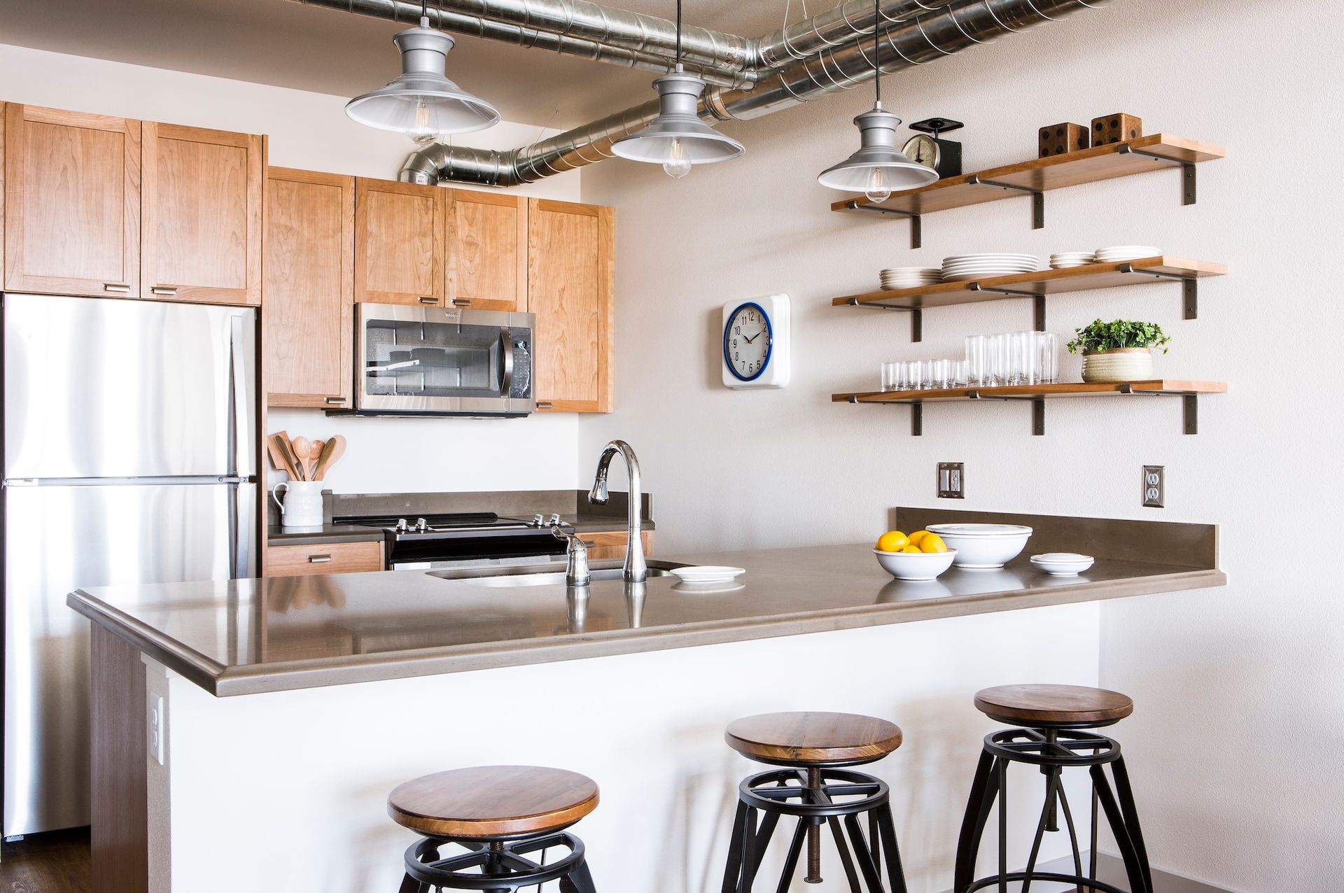 Modern kitchen with stainless steel appliances, island, bar stools, and wall shelves with decor