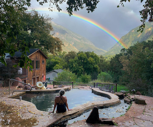 A woman is sitting in a pool with a rainbow in the background in Avalanche Ranch Hot Springs