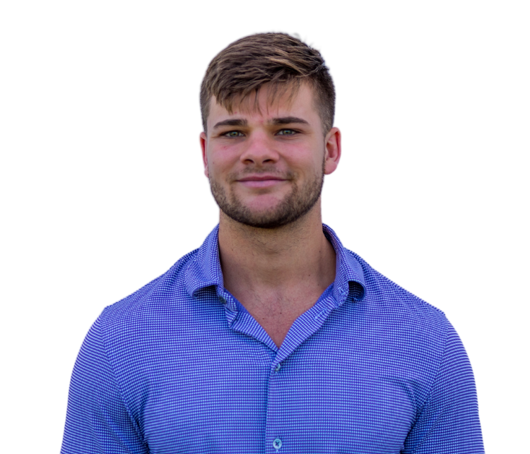 A person with short brown hair and light stubble, wearing a blue patterned button-down shirt against a white background.