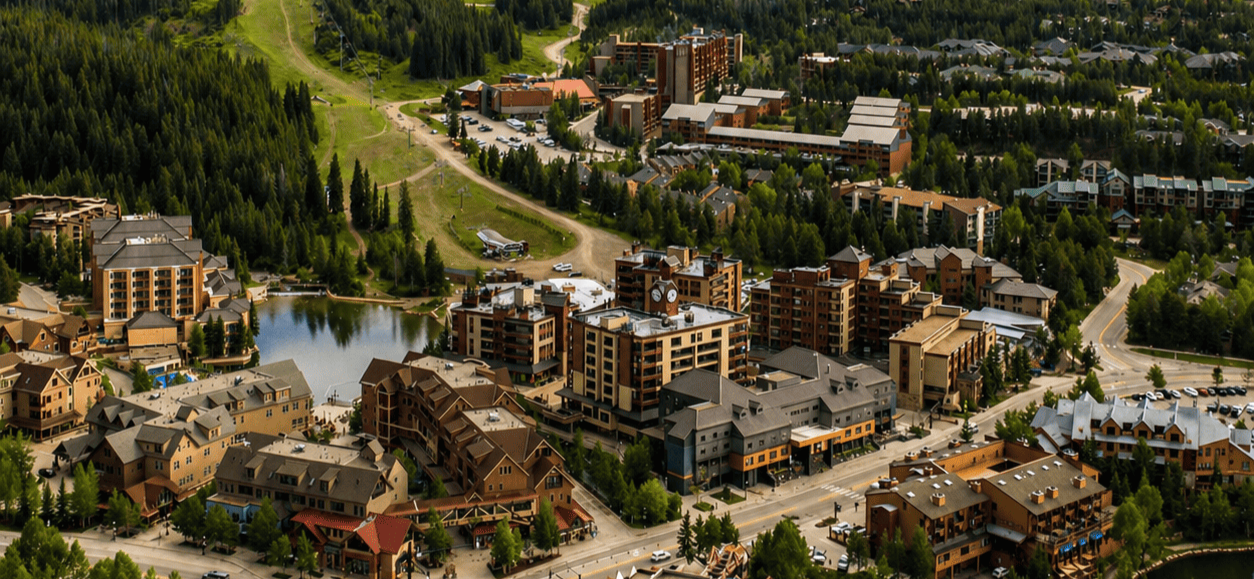Aerial view of a mountain resort town with hotels, forested hills, and a small lake