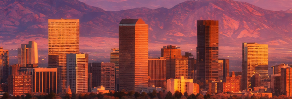 Sunset city skyline with tall modern buildings glowing orange against purple mountains