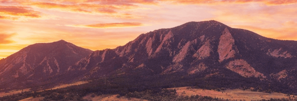 Sunset over rugged mountain range with pink-orange sky and dark rocky slopes