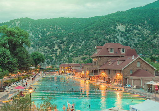 A large swimming pool surrounded by buildings and trees with mountains in the background in Glenwood Hot Springs Colorado