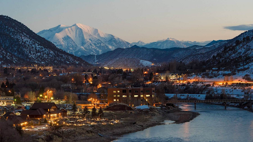 A city with mountains in the background and a river in the foreground in Iron Mountain Hot Springs Colorado 