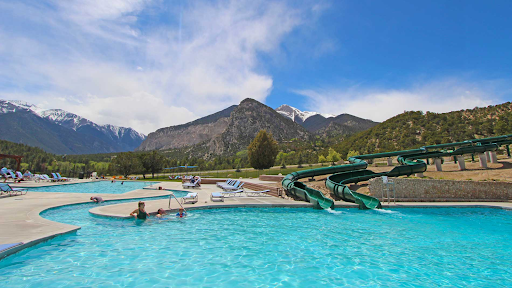 A swimming pool with a water slide and mountains in the background in Mount Princeton Hot Springs Colorado