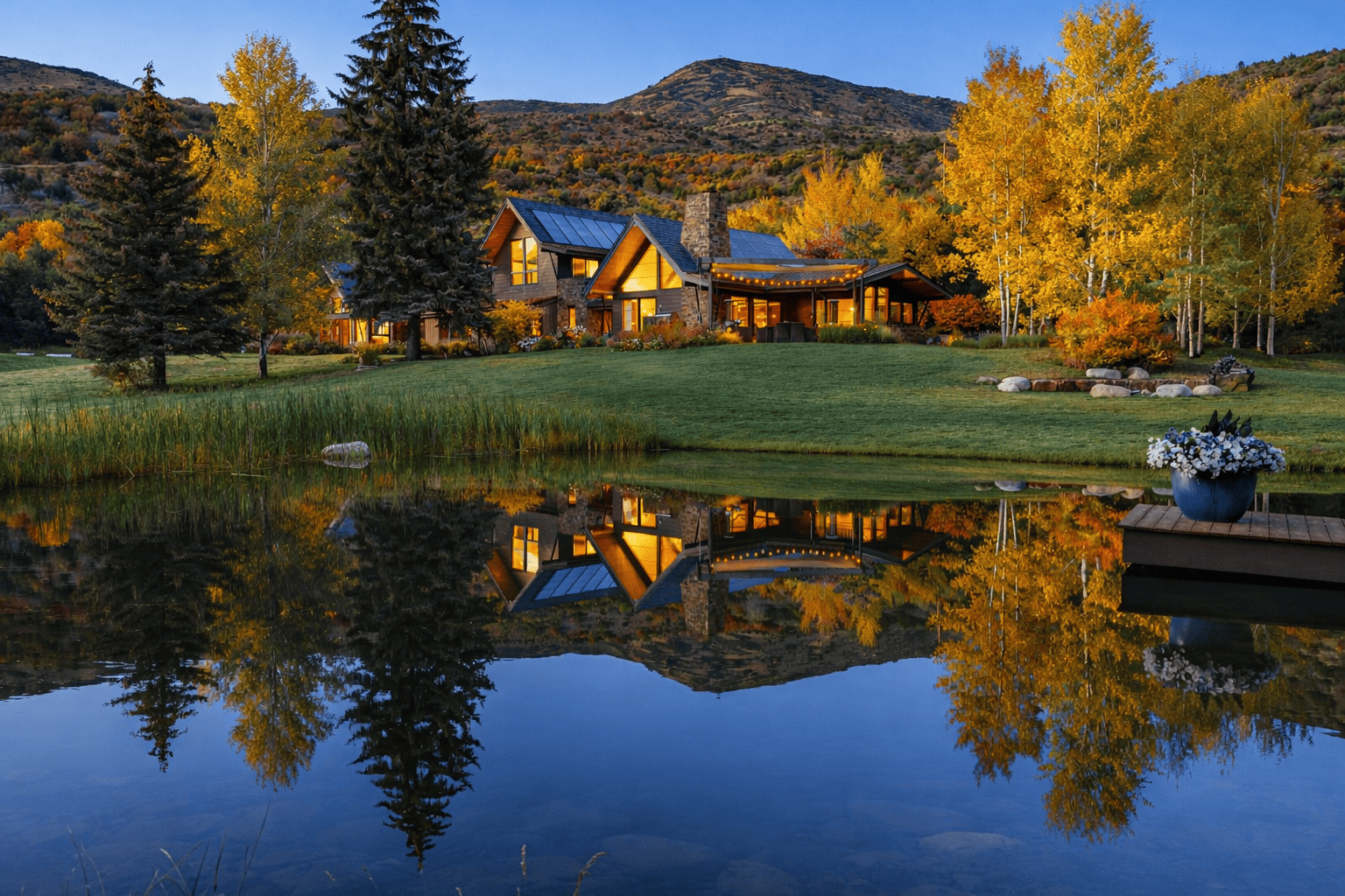 A rustic home in Snowmass, CO, nestled among golden autumn trees sits behind a still pond, reflecting the house and trees in the water.