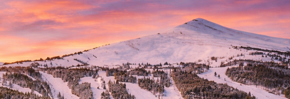 Snow-covered mountain at sunset with pink sky and scattered trees on the slopes