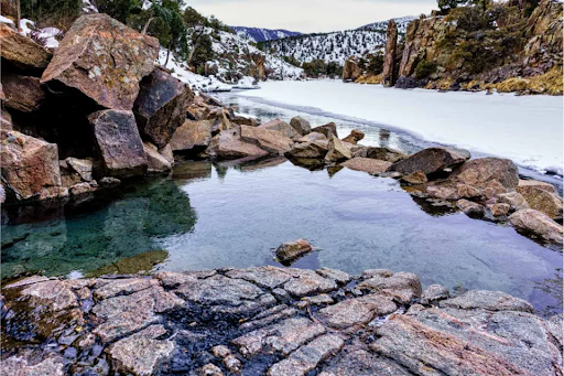 A pool of water surrounded by rocks and snow in the mountains in Radium Hot Springs Colorado
