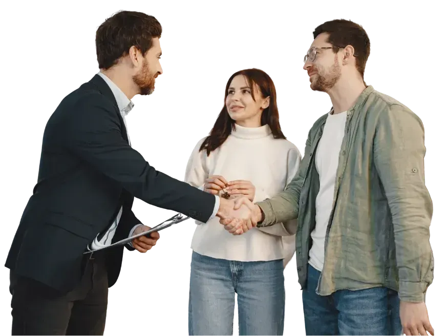 A professional in a suit shakes hands with a person while another person looks on, suggesting a real estate agreement.